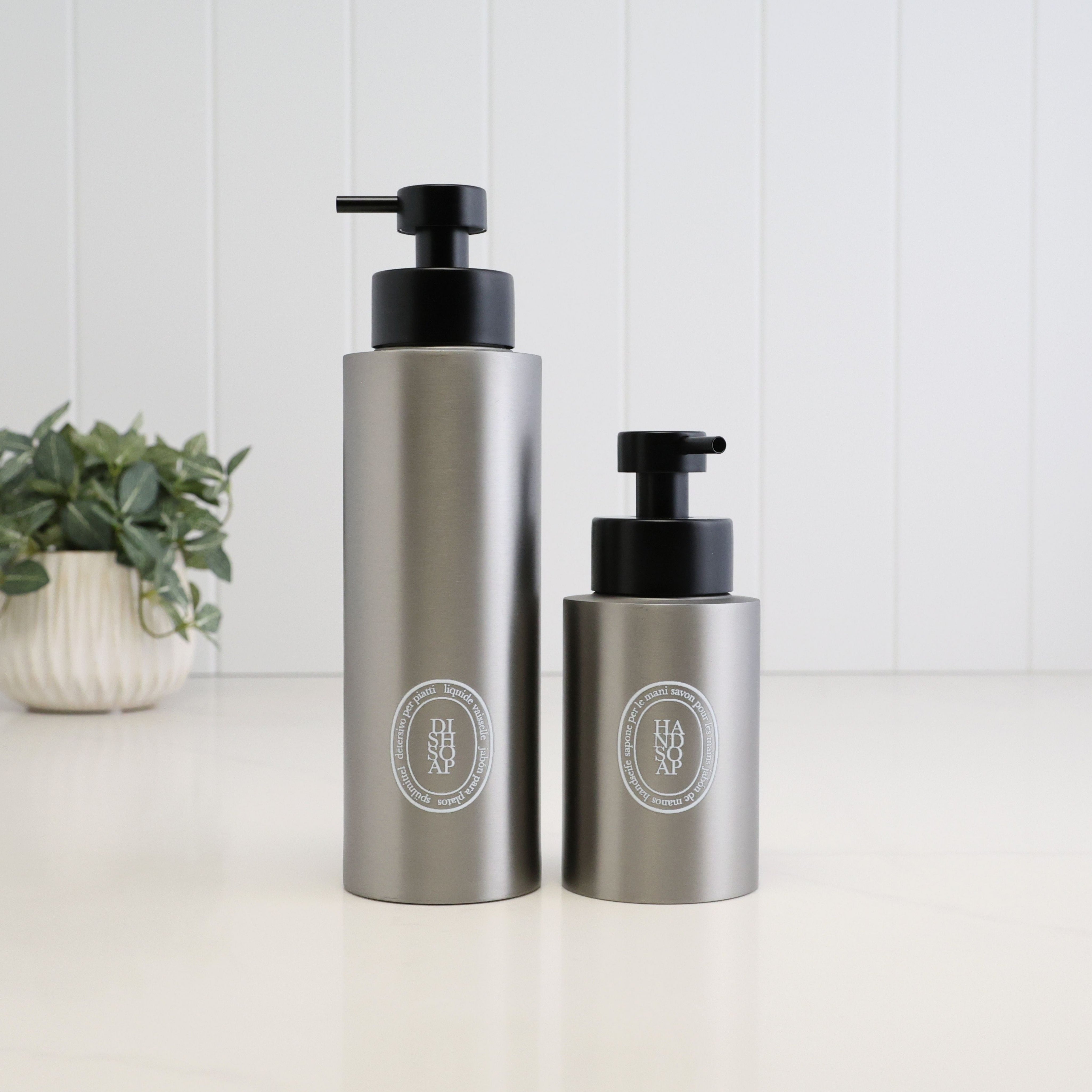 500ml and 250ml brushed 304 stainless steel soap dispensers with white round labels and satin black liquid pumps, shown together to compare the two bottle sizes.