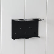 Loopa double wall-mounted soap dispenser bracket in black powder-coated aluminium, securely installed on a white panelled wall. Featuring two circular bottle openings and a supporting base, this minimalist metal holder accommodates two Loopa 250ml or 500ml refillable dispenser bottles. Ideal for organising hand soap and lotion in bathrooms or shampoo and conditioner in showers.