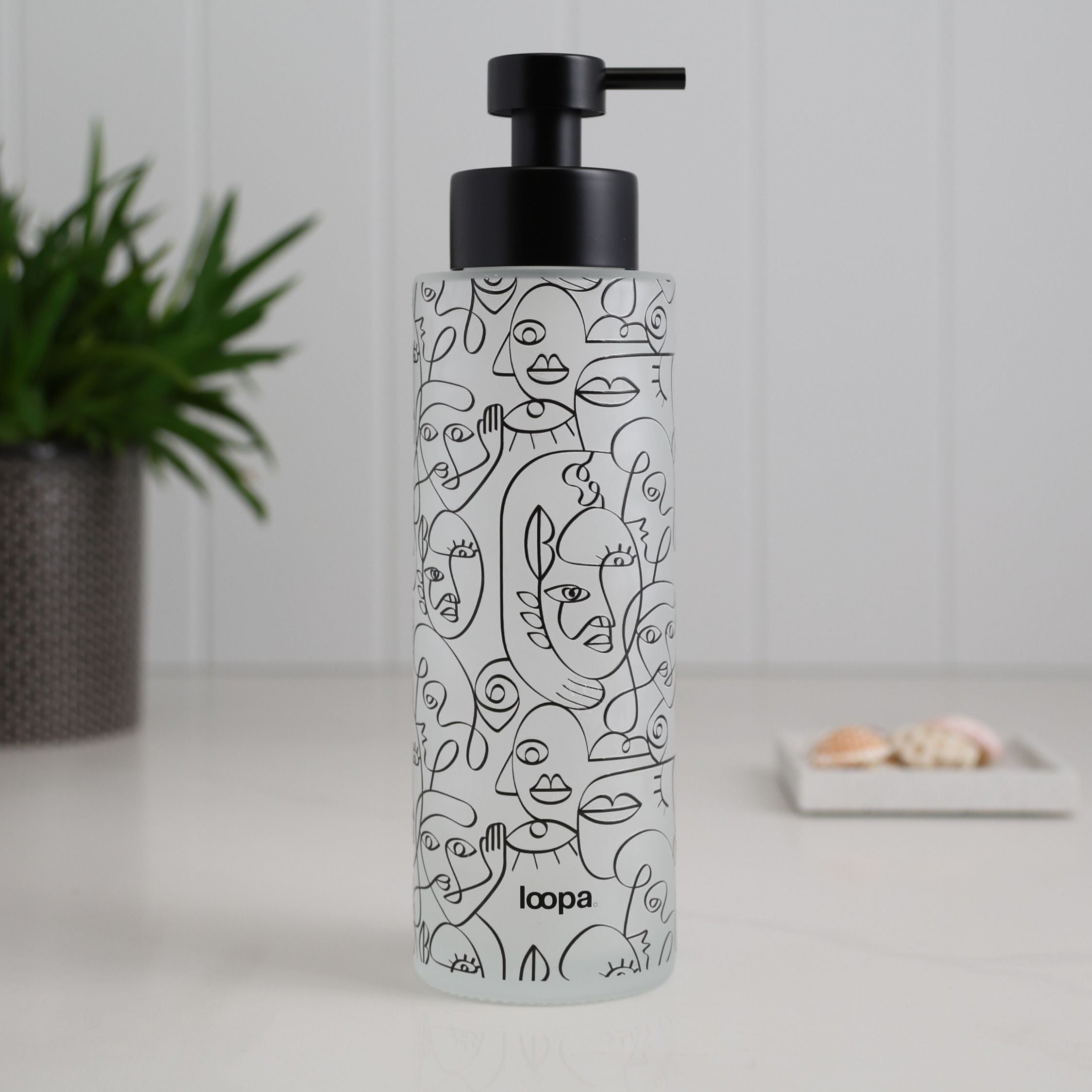 Frosted glass bottle dispenser with a black wrap label, presented as a refillable option for contemporary kitchens or bathrooms