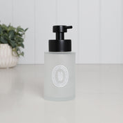 250ml frosted glass hand soap dispenser with white oval label and satin black stainless steel liquid pump, styled on a clean bathroom countertop.