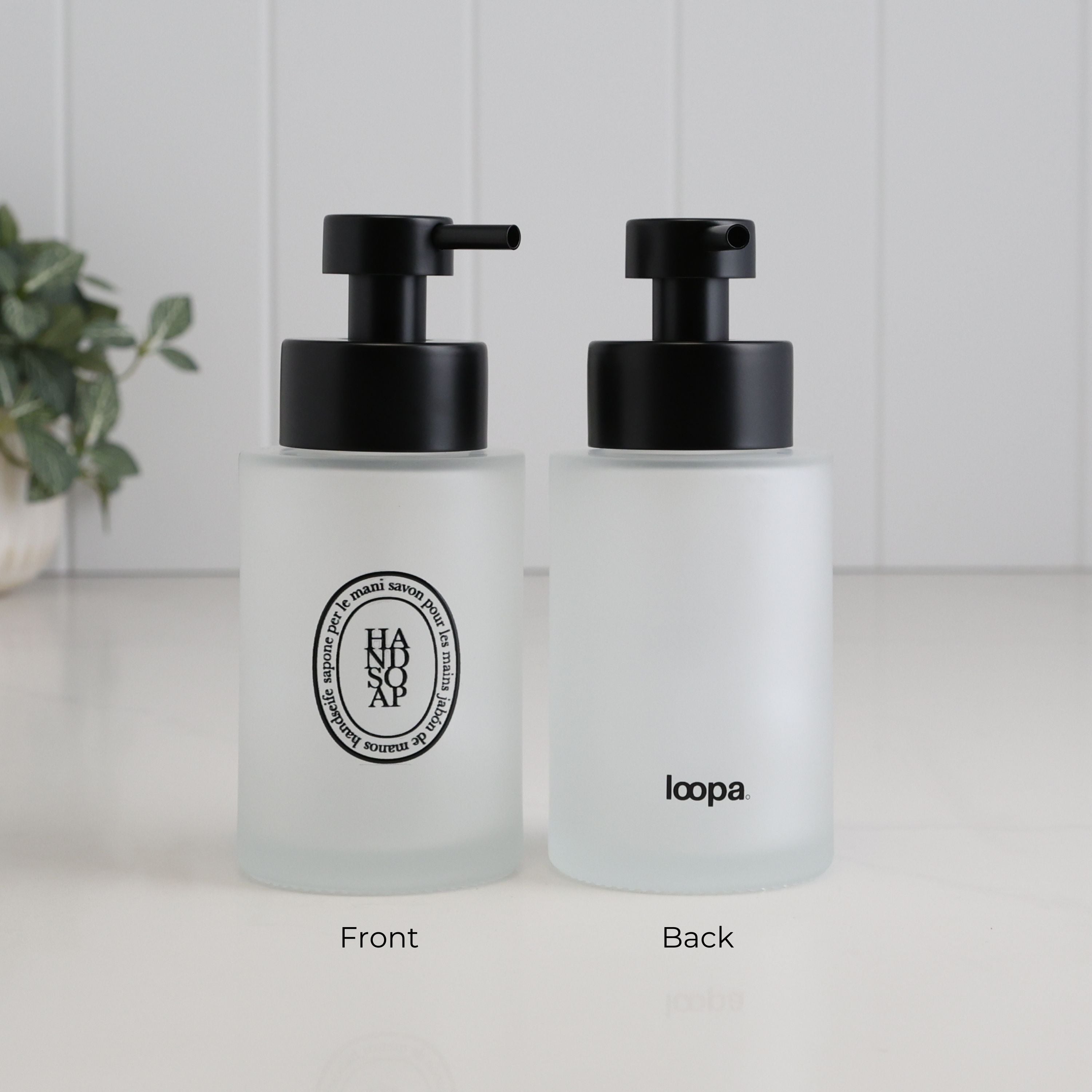 Front and back view of a frosted glass hand soap dispenser with black oval Hand Soap label, satin black pump and Loopa branding on the reverse.