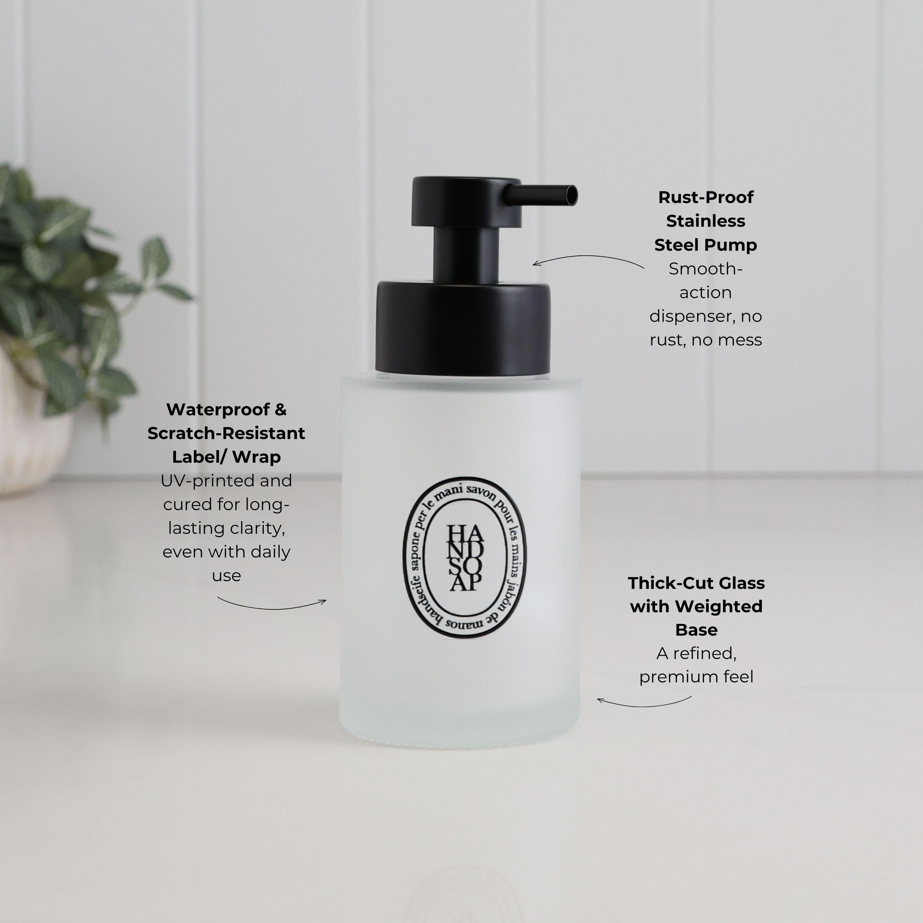 A frosted glass pump bottle with a black dispenser, shown on a white surface with white paneled walls in the background. Text callouts describe features such as a waterproof and scratch-resistant label wrap, rust-proof stainless steel pump, thick-cut glass with weighted base, and smooth action dispenser.