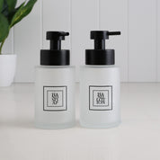 Set of two 250ml frosted glass soap dispensers for hand soap and hand lotion, featuring black square labels and satin black stainless steel liquid pumps for bathroom or kitchen use.