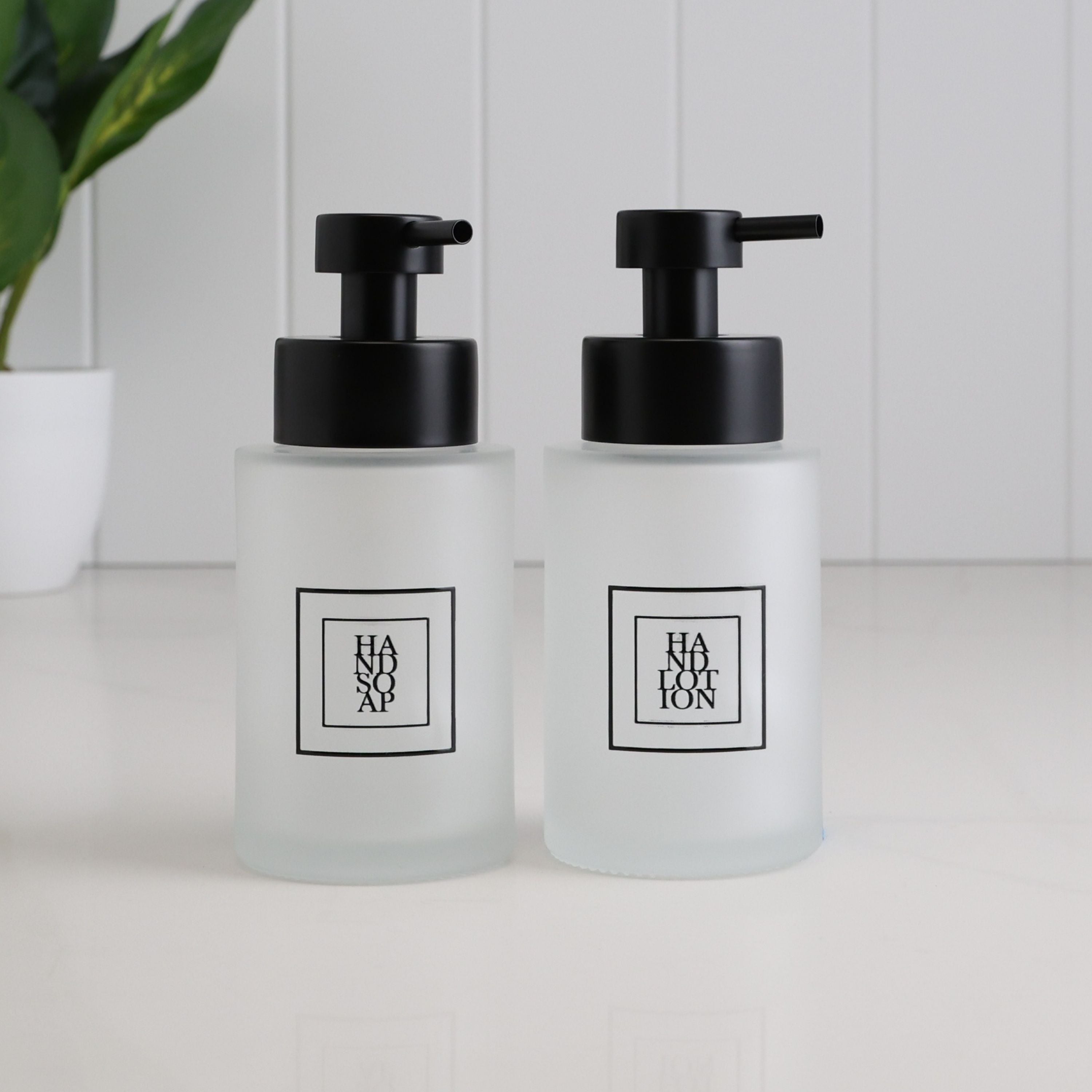 Set of two 250ml frosted glass soap dispensers for hand soap and hand lotion, featuring black square labels and satin black stainless steel liquid pumps for bathroom or kitchen use.