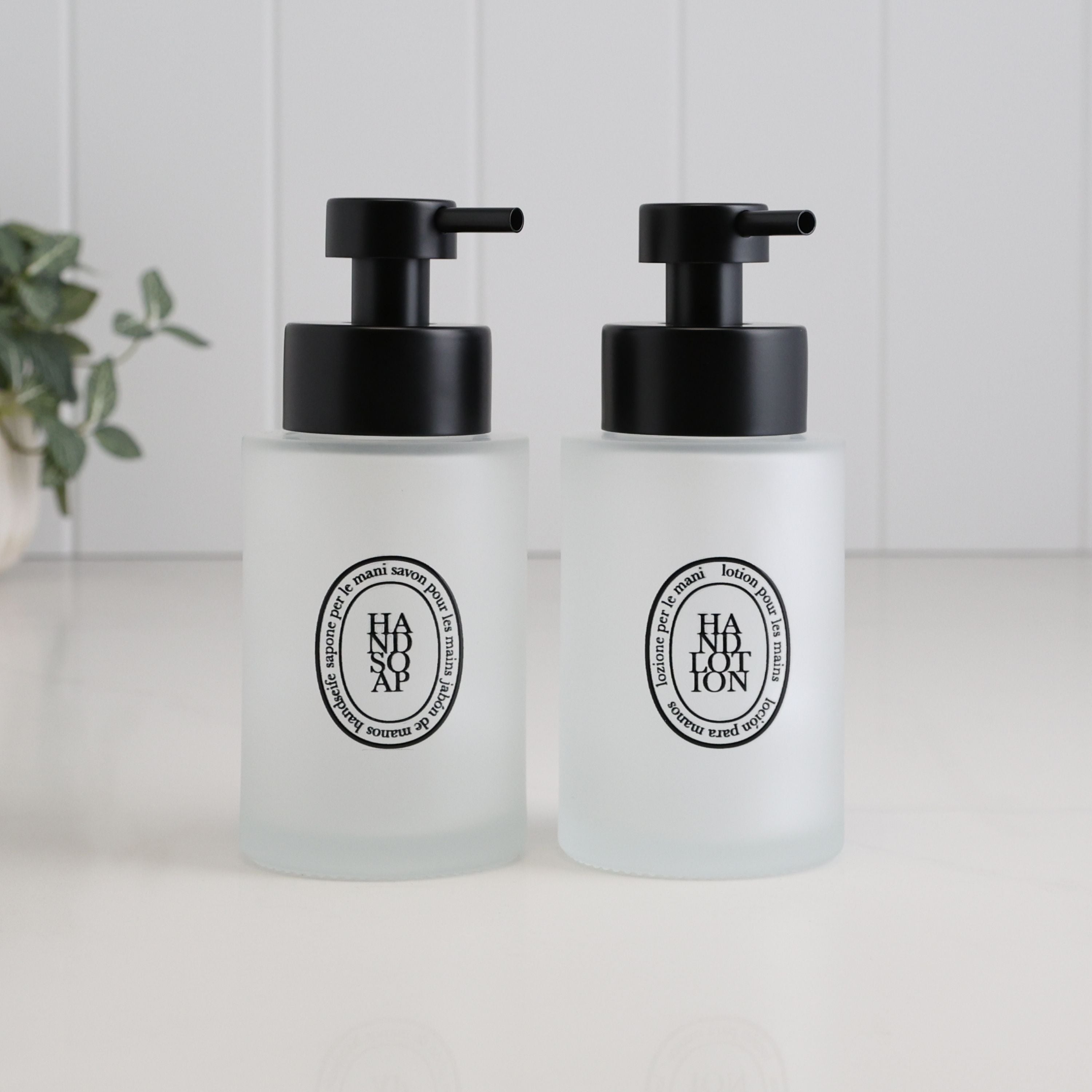 Set of two frosted glass soap dispensers with black oval Hand Soap and Hand Lotion labels, finished with satin black pumps for a coordinated bathroom sink or ensuite.