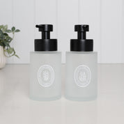 Set of two 250ml frosted glass soap dispensers for hand soap and hand lotion, with white oval labels and satin black stainless steel pumps.