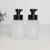 Pair of 250ml frosted glass soap dispensers with white square Hand Soap and Hand Lotion labels and satin black pumps, designed as matching refillable bathroom bottles for a sink or vanity.