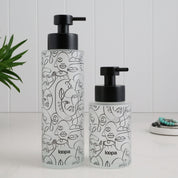 Frosted glass dispenser bottle with a black wrap label, designed for refillable soap or lotion in modern home spaces