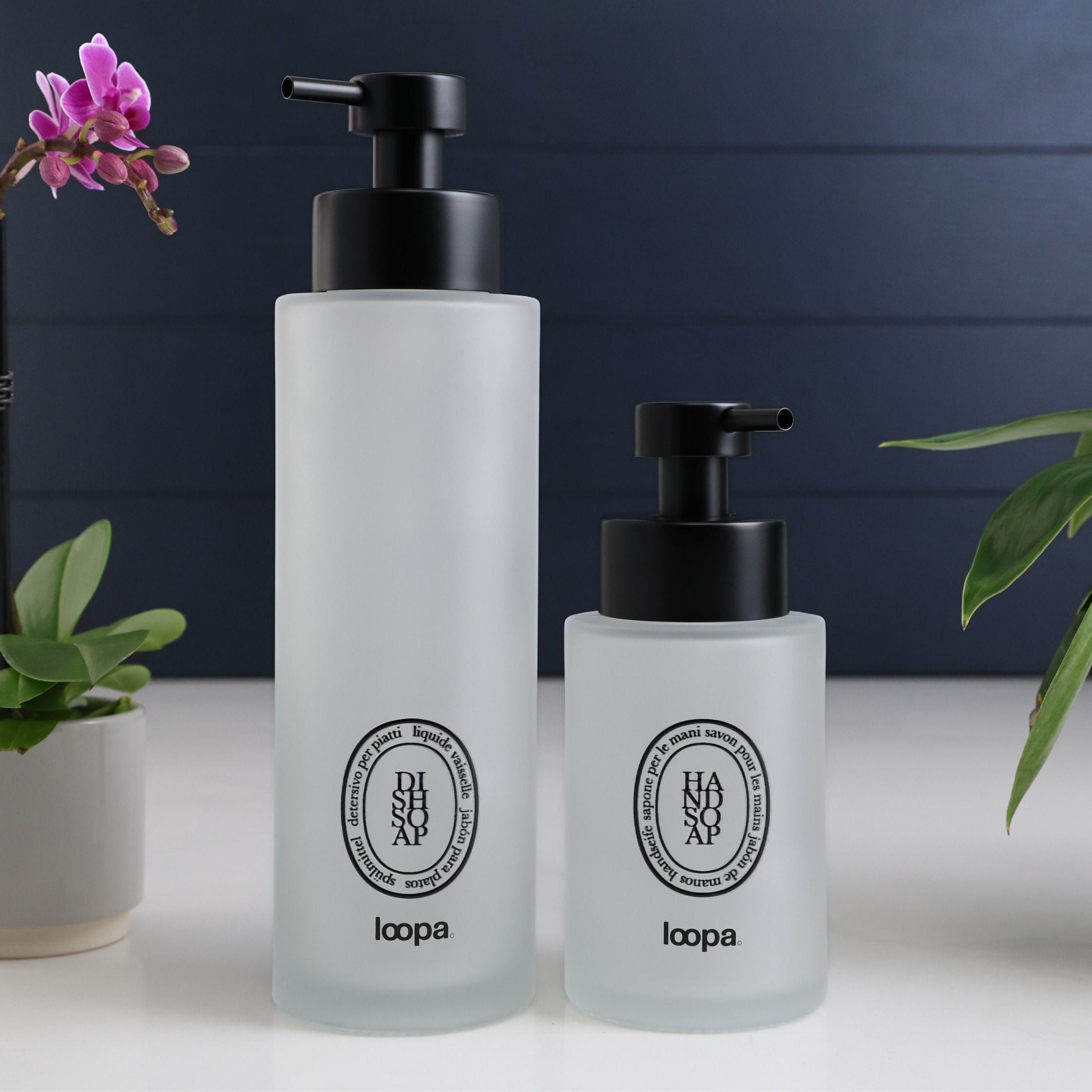 Frosted glass round bottle dispenser with a black oval label, designed for refillable soap or lotion in modern kitchen or bathroom spaces