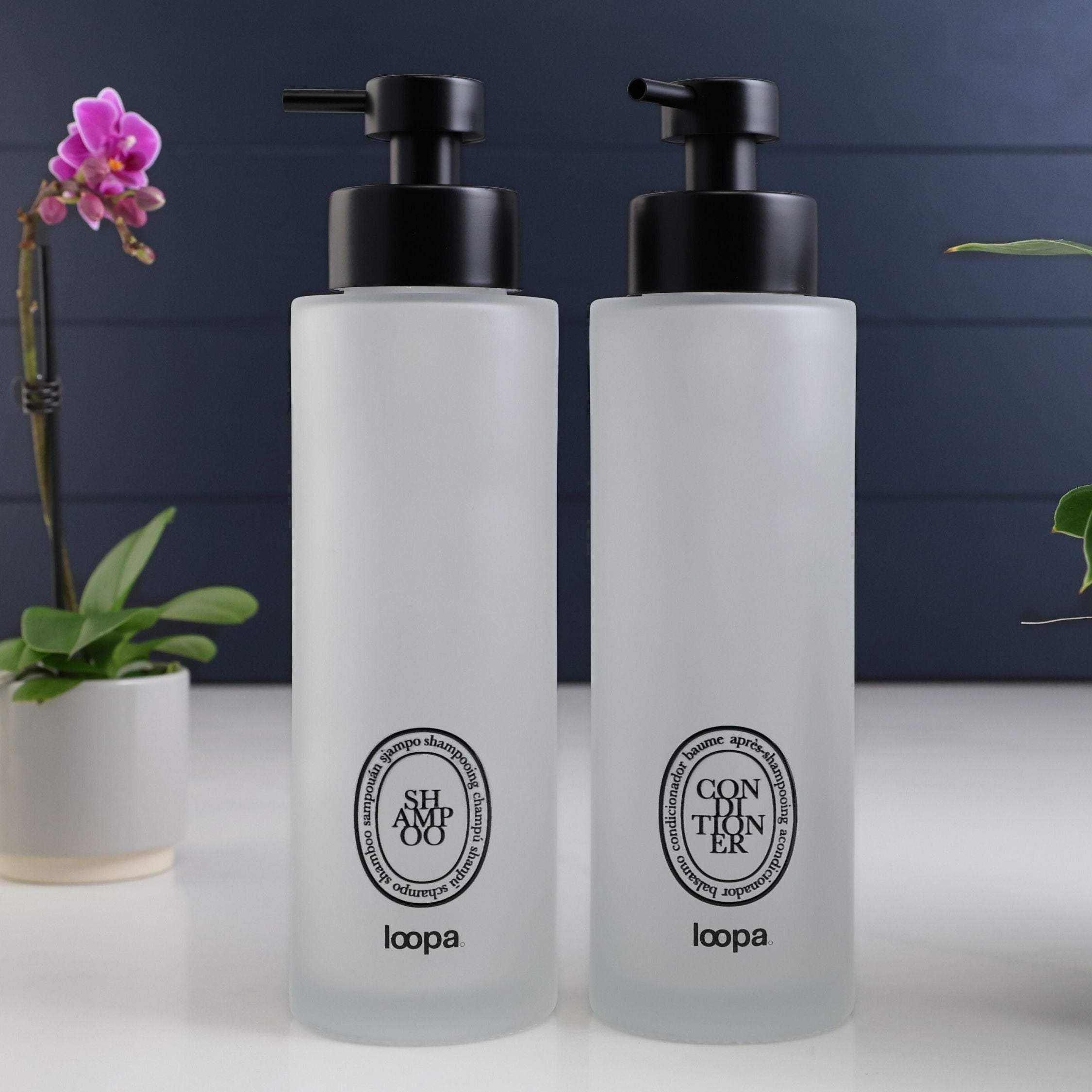 Frosted glass round bottle dispenser with a black oval label, presented as a refillable choice for everyday soap or lotion use