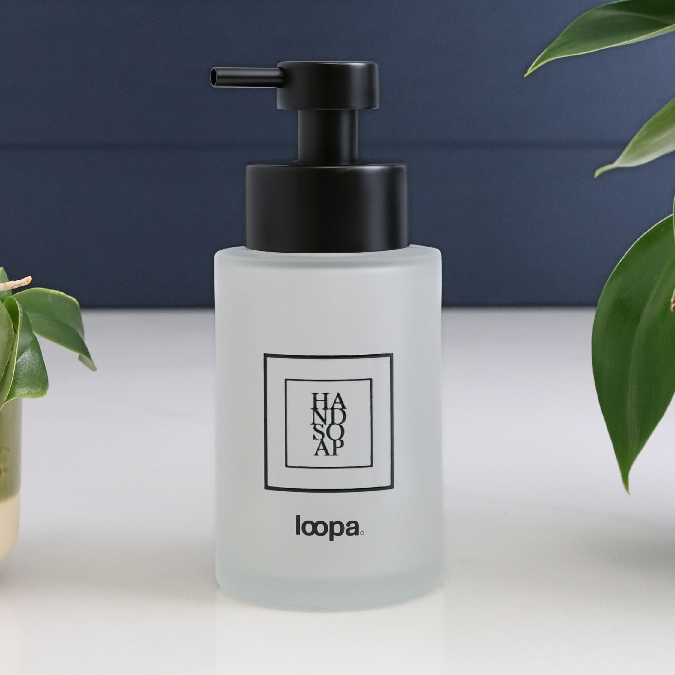 Frosted glass round bottle dispenser with a black square label, designed for refillable soap or lotion in modern home settings