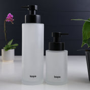 Two frosted glass round bottle dispensers shown together in 500ml and 250ml refillable sizes, styled for use across kitchens, bathrooms, or cloakroom spaces