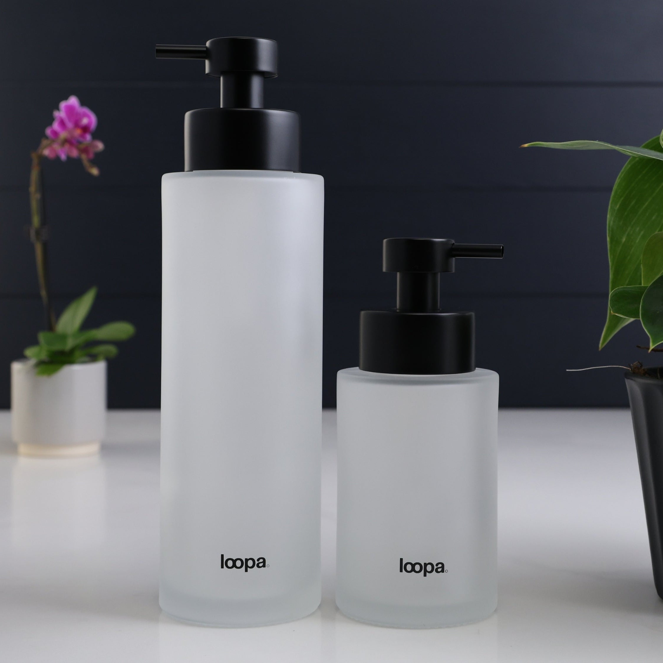 Two frosted glass round bottle dispensers shown together in 500ml and 250ml refillable sizes, styled for use across kitchens, bathrooms, or cloakroom spaces