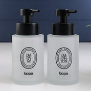Two frosted glass round bottle dispensers with black oval labels, shown as matching 250ml refillable options for soap or lotion