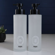 Frosted glass round bottle dispenser with a white oval label, presented as a refillable option for everyday soap or lotion use