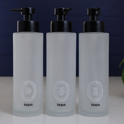 Tall frosted glass round bottle dispenser with a white oval label, created for refillable soap or lotion in contemporary home spaces