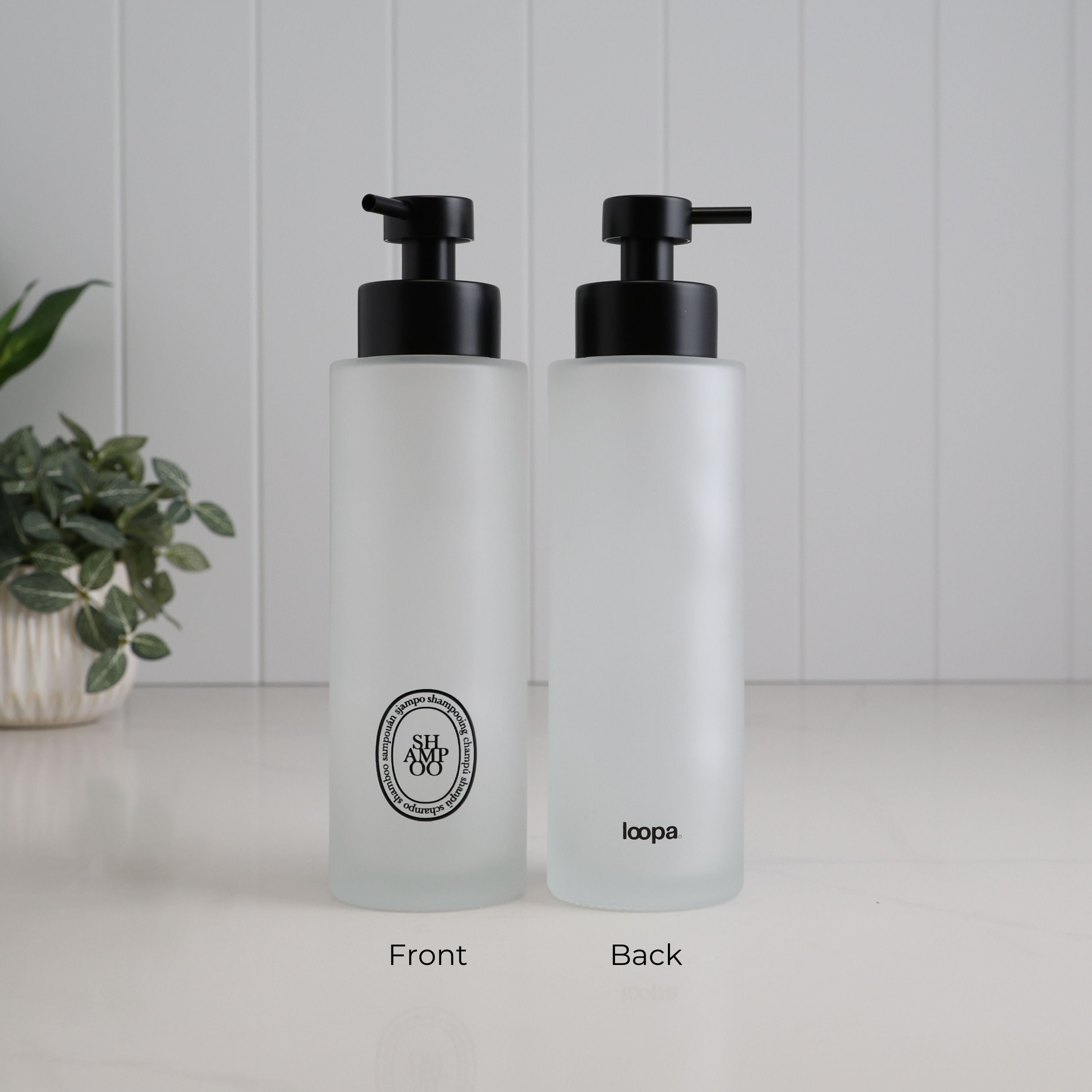 Front and back view of a 500ml frosted glass shampoo dispenser with black oval label, satin black pump and Loopa branding, designed as a refillable bathroom and shower soap dispenser.