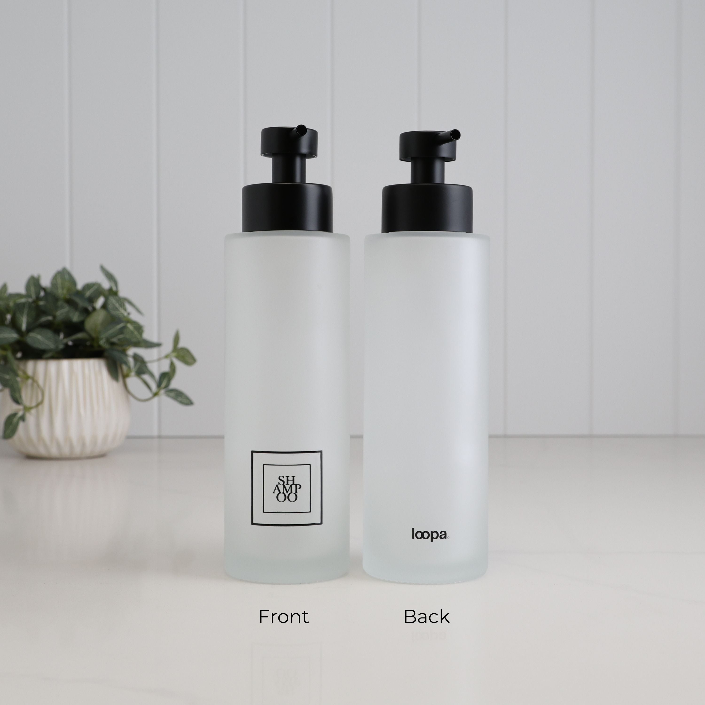 Front and back view of a 500ml frosted glass shampoo dispenser with black square label, Loopa branding and satin black stainless steel liquid pump.