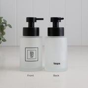 Front and back view of a frosted glass hand soap dispenser with black square label, Loopa branding and satin black stainless steel pump.