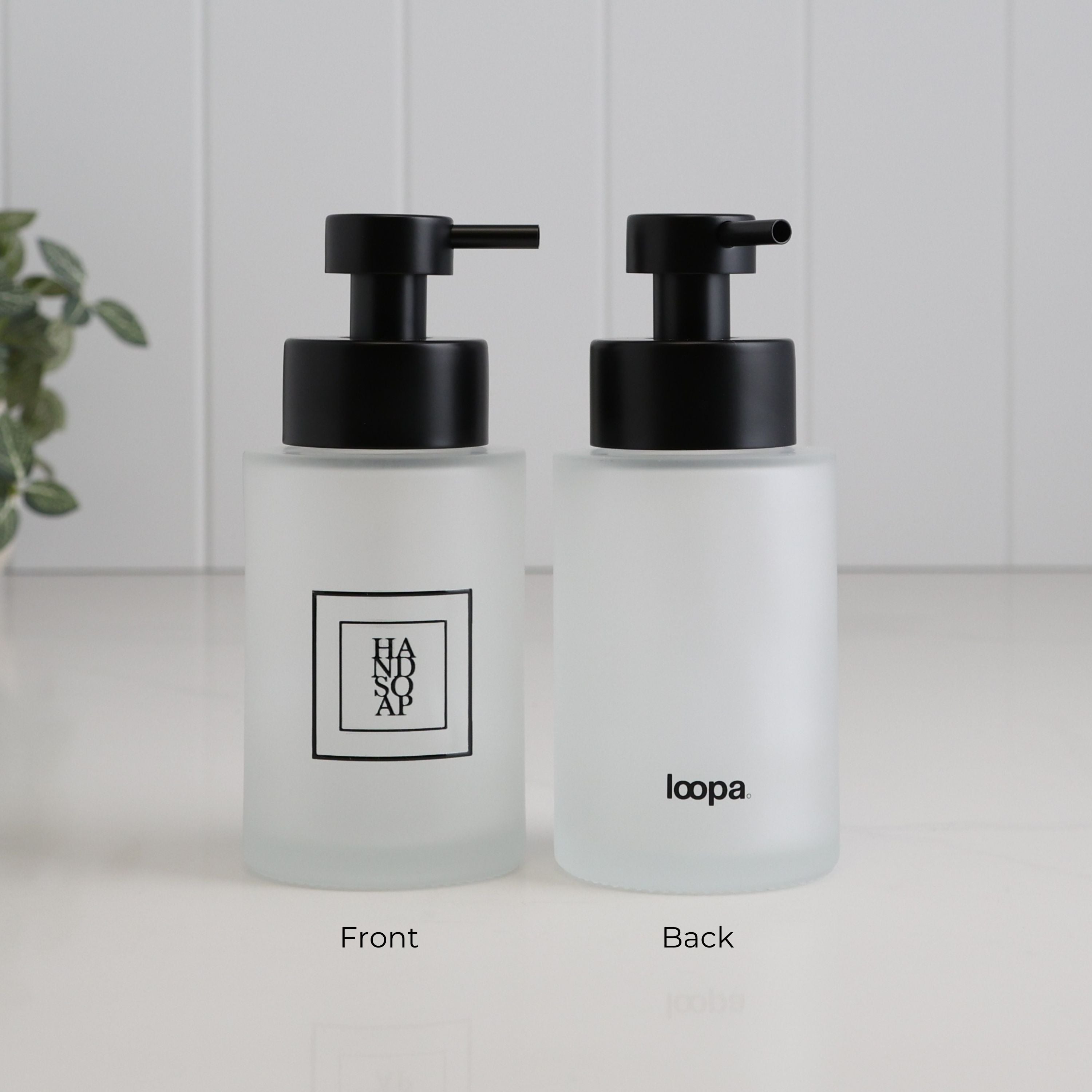 Front and back view of a frosted glass hand soap dispenser with black square label, Loopa branding and satin black stainless steel pump.