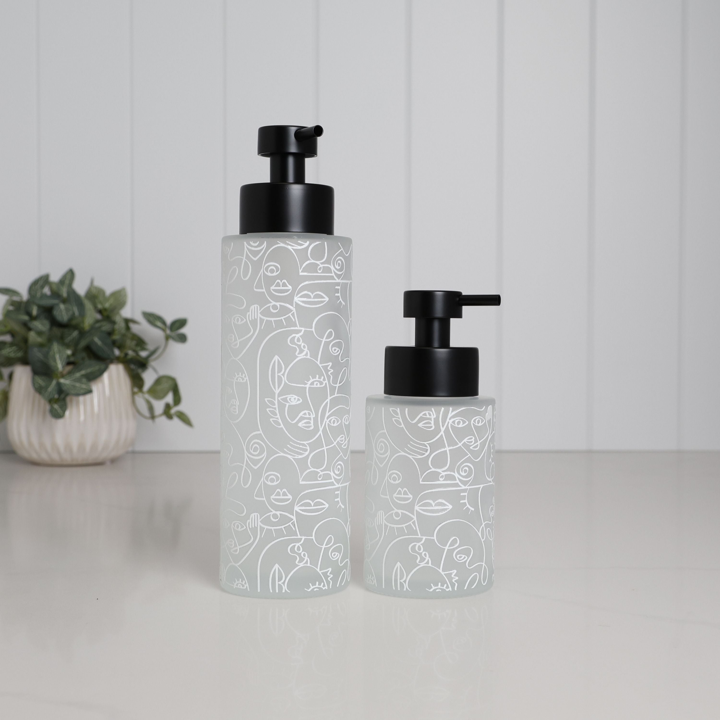Frosted glass soap dispenser set with abstract face line art design, 500ml and 250ml refillable pump bottles with matte black stainless steel pumps, modern bathroom decor accessories for hand soap lotion or shampoo, artistic reusable glass dispensers for stylish sink or vanity setup, minimalist luxury homeware set with decorative printed finish