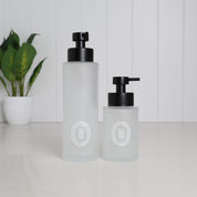 250ml and 500ml frosted glass soap dispensers with white circular labels and satin black stainless steel pumps, shown together for size comparison.