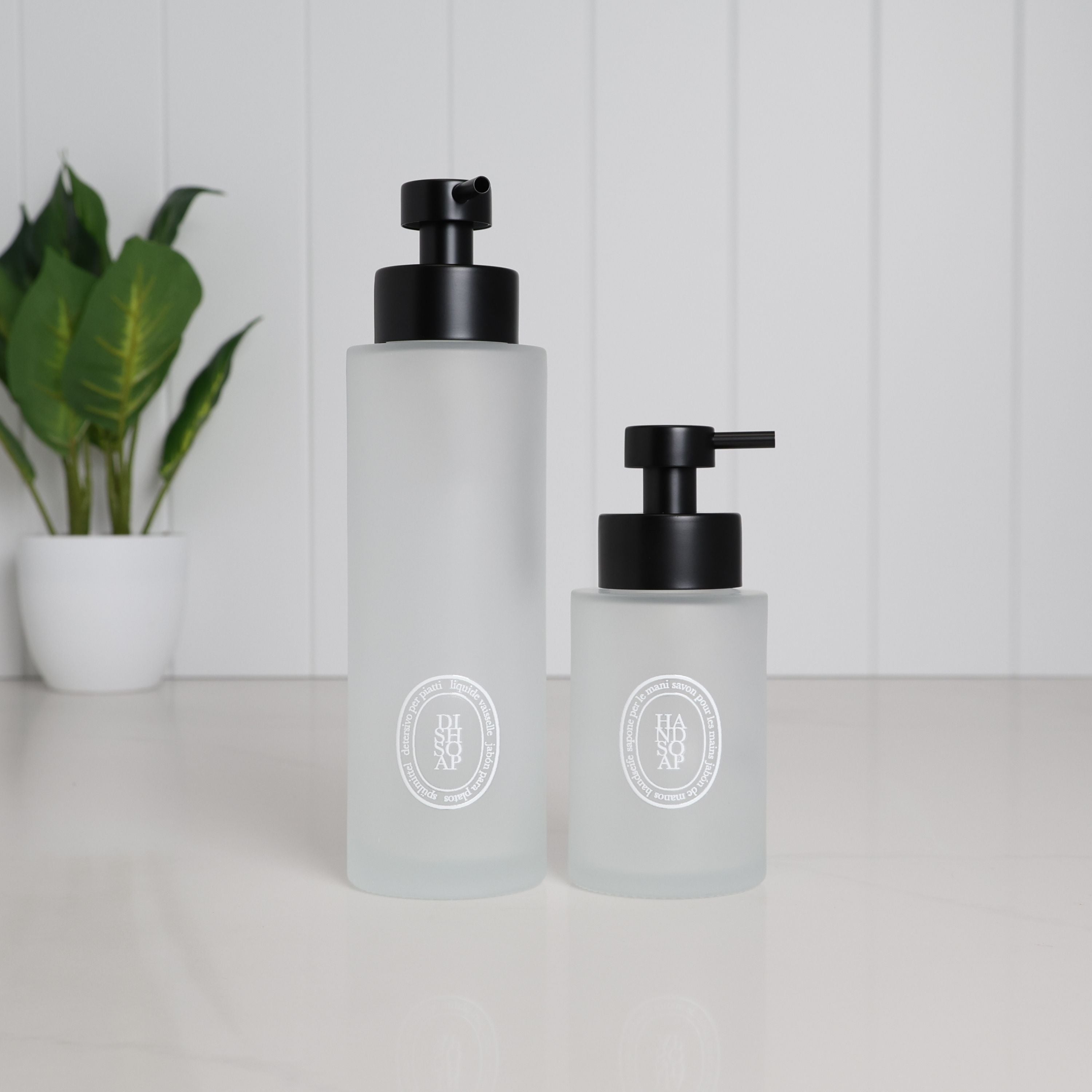 250ml and 500ml frosted glass soap dispensers with white circular labels and satin black stainless steel pumps, shown together for size comparison.