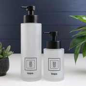 Square frosted glass bottle dispenser with a black label, presented as a refillable option for modern kitchen or bathroom use