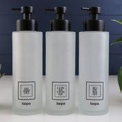Tall square frosted glass dispenser bottle with a black label, designed for refillable soap or lotion in contemporary home spaces