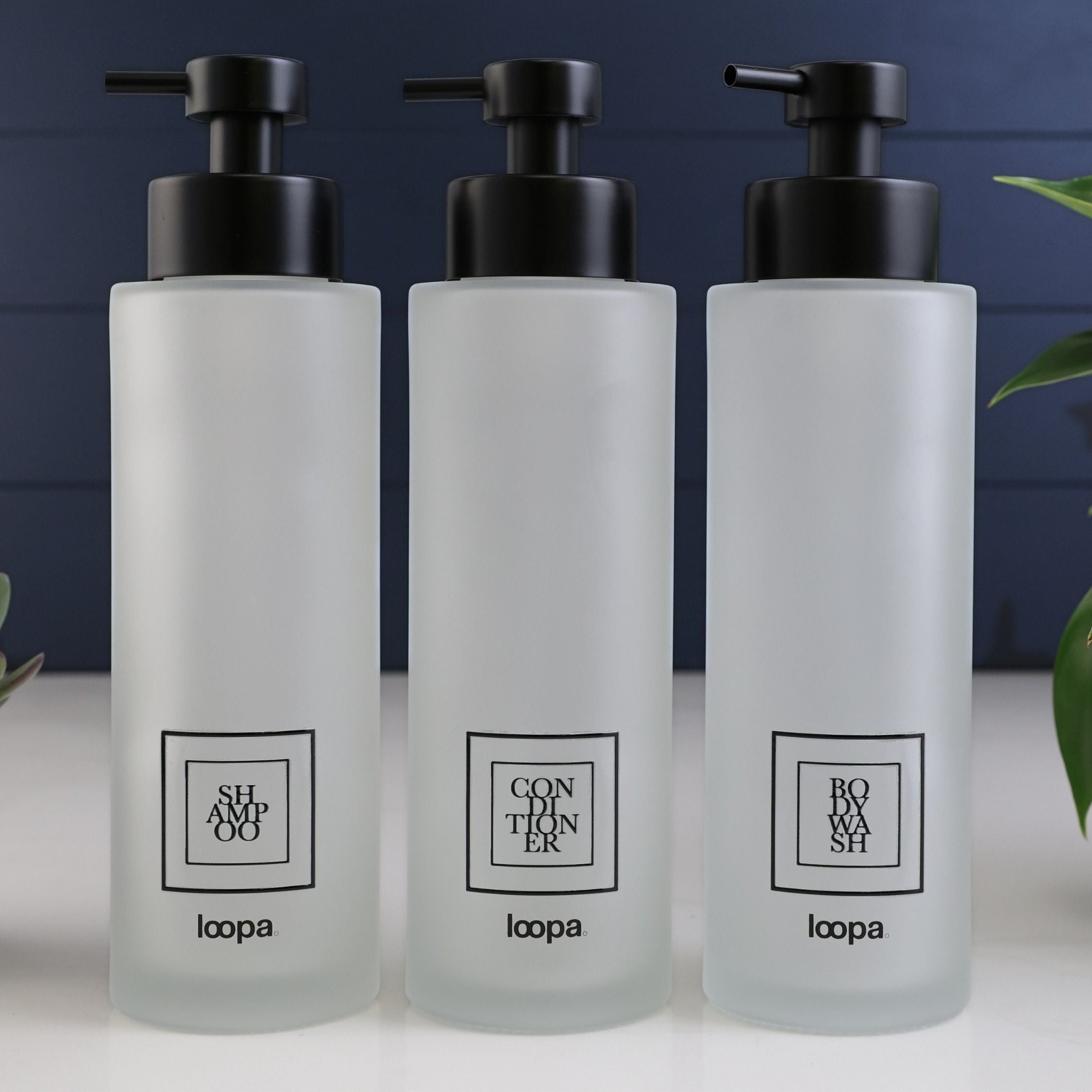 Tall square frosted glass dispenser bottle with a black label, designed for refillable soap or lotion in contemporary home spaces