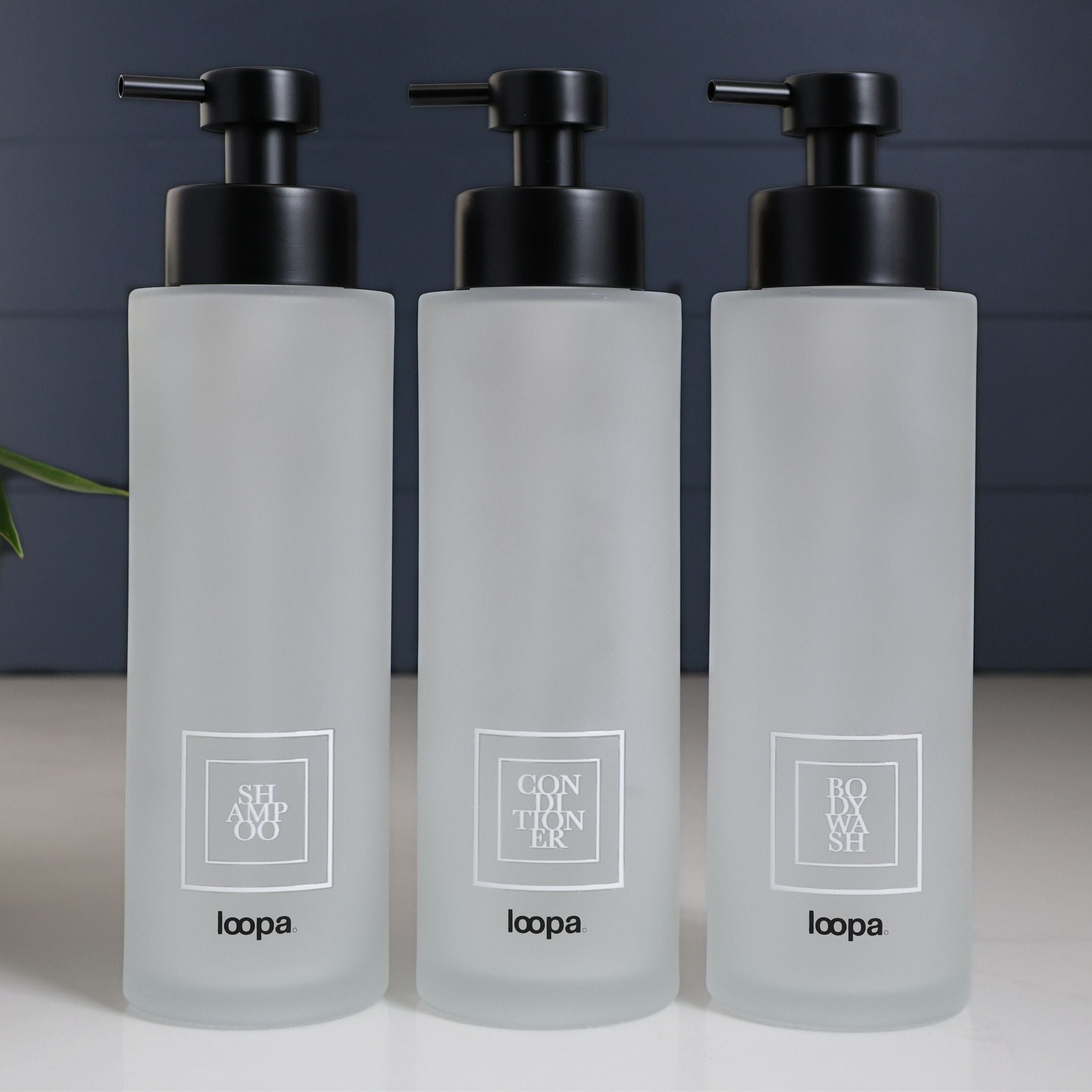 Tall square frosted glass bottle dispenser with a white label, designed for refillable soap or lotion in modern home settings