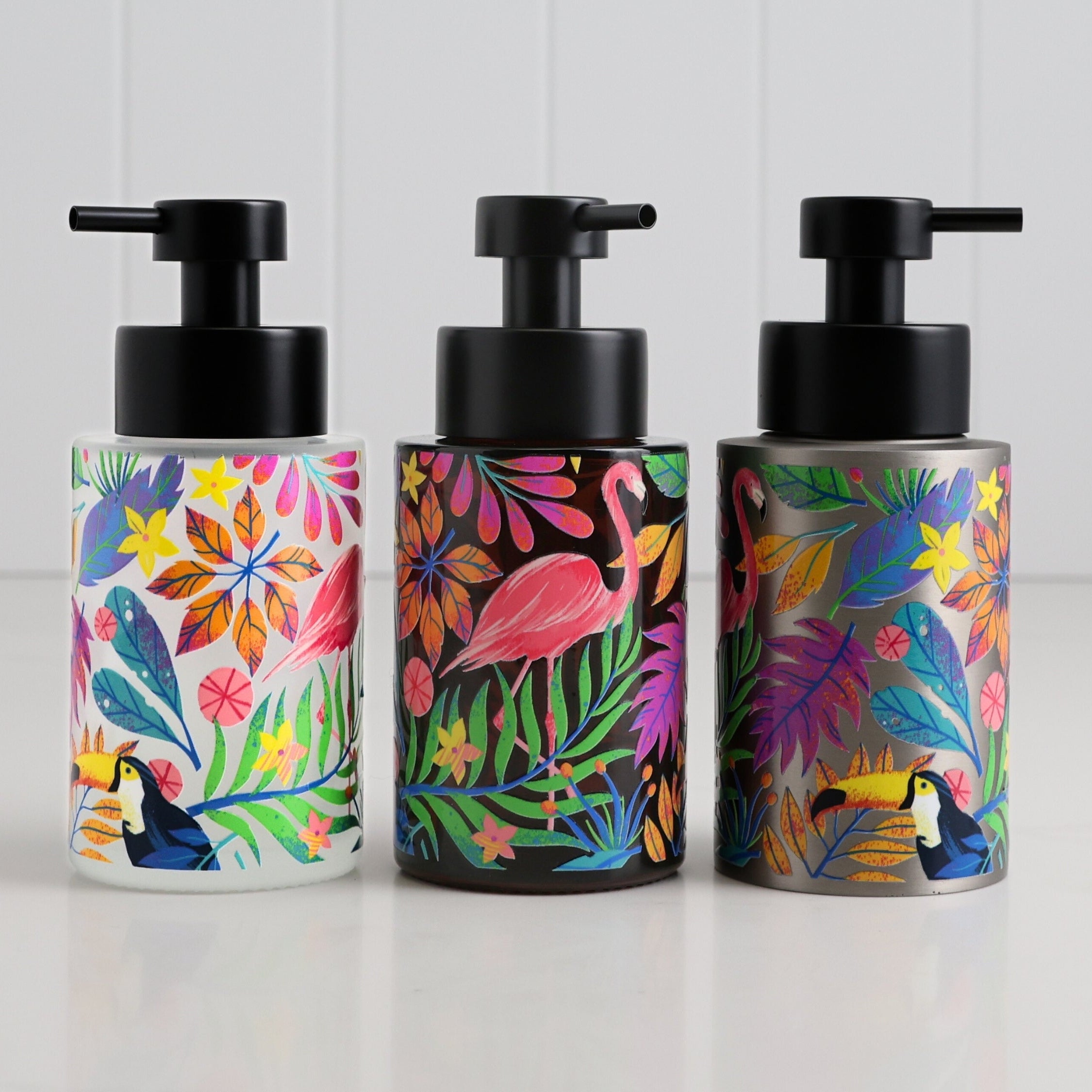 Three glass round bottle dispensers with tropical flamingo wrap artwork, shown as matching 250ml refillable bottles for soap or lotion use