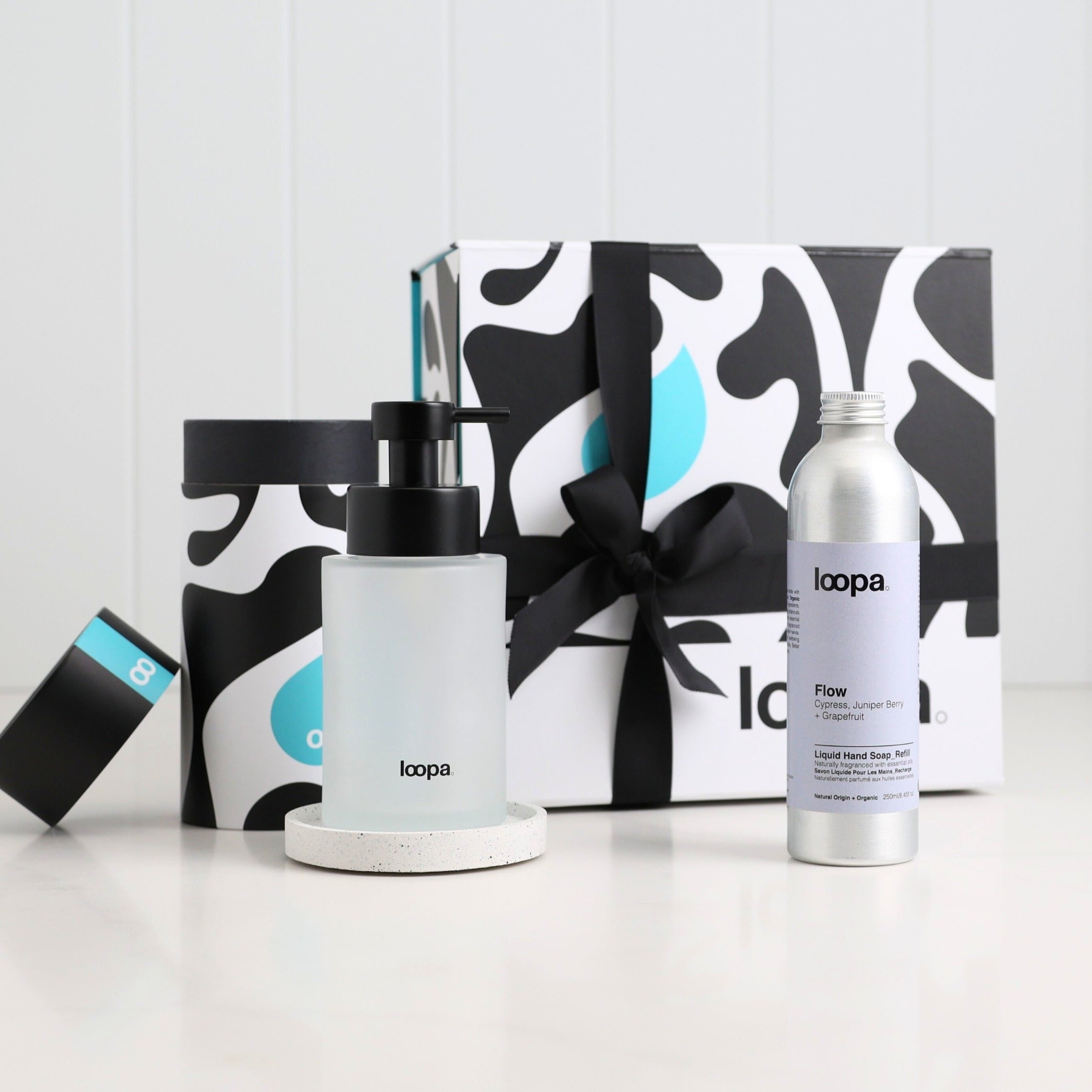 Frosted refillable soap dispenser with black pump and terrazzo-style base displayed beside a Flow scent aluminium refill bottle, styled with Loopa’s bold gift packaging and ribbon for a fresh, modern luxury gifting look.