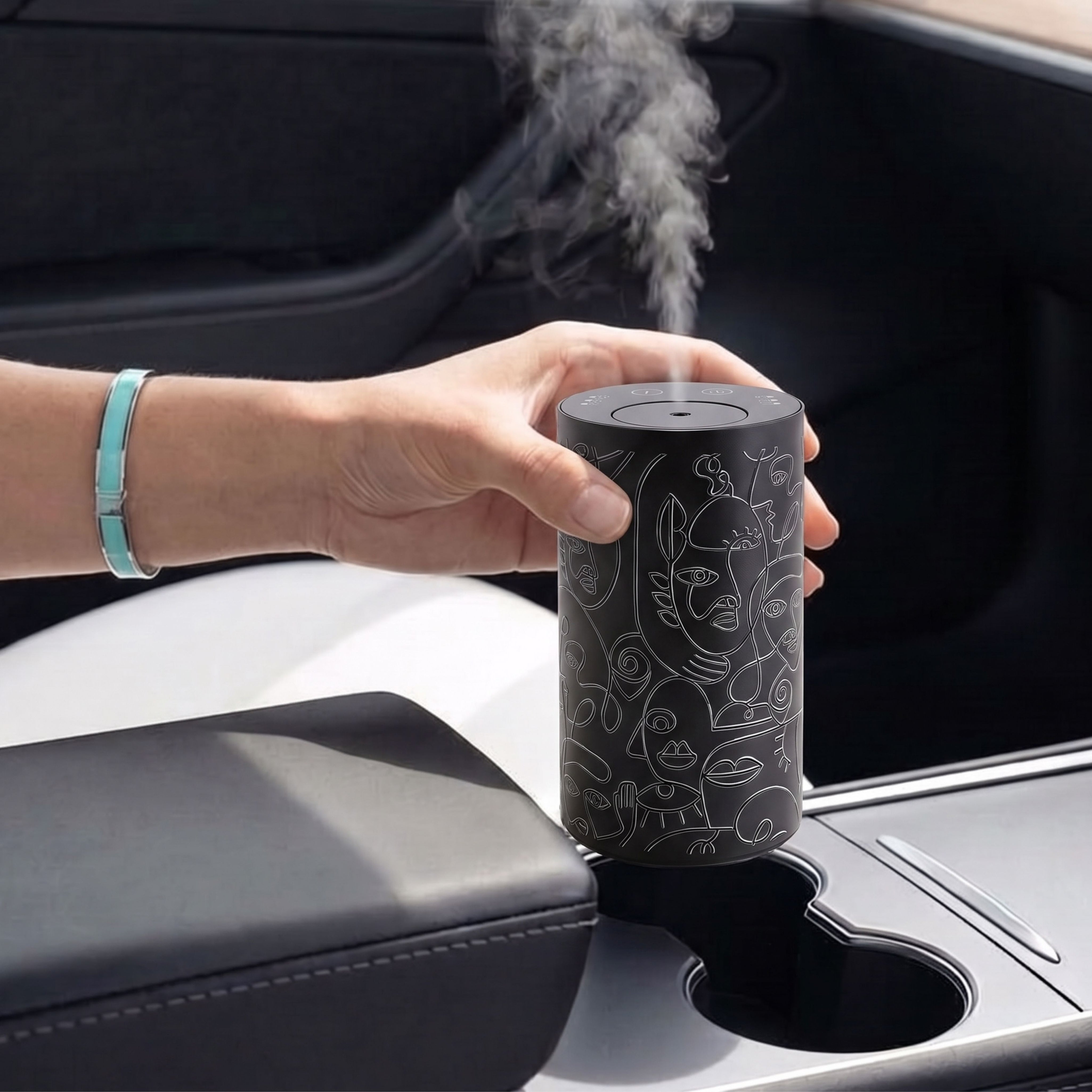 Loopa cordless waterless essential oil diffuser in black with abstract grey line art, shown inside a car cup holder releasing a fine fragrance mist. Compact rechargeable aromatherapy diffuser designed for portable use without water or heat.