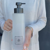 500ml frosted glass shampoo dispenser with black square label and satin black stainless steel pump, shown held in hand to demonstrate the tall refillable bottle size and premium bathroom design.