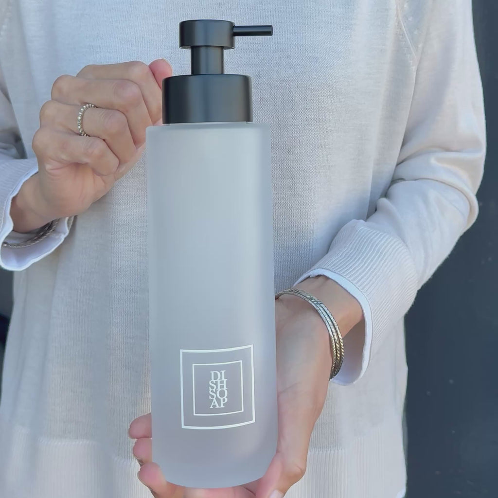 500ml frosted glass soap dispenser with white Dish Soap label and satin black pump, shown held in hand to demonstrate the tall refillable bottle size for a modern kitchen sink or countertop.