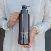Video showing a 500ml amber glass conditioner dispenser with a white square label and satin black pump, held to show the bottle’s size and design.