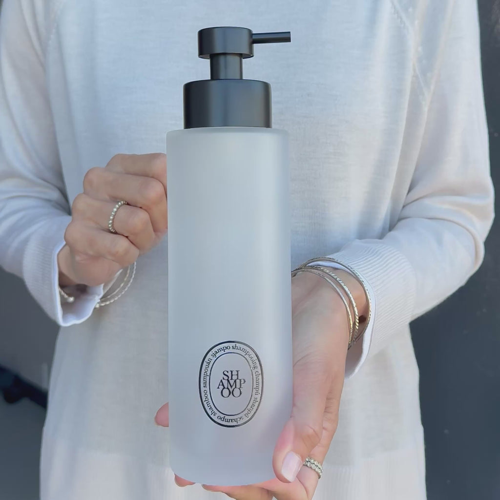 Video showing a 500ml frosted glass shampoo dispenser with black oval Shampoo label and satin black pump, demonstrating the size and finish of the refillable bathroom bottle.