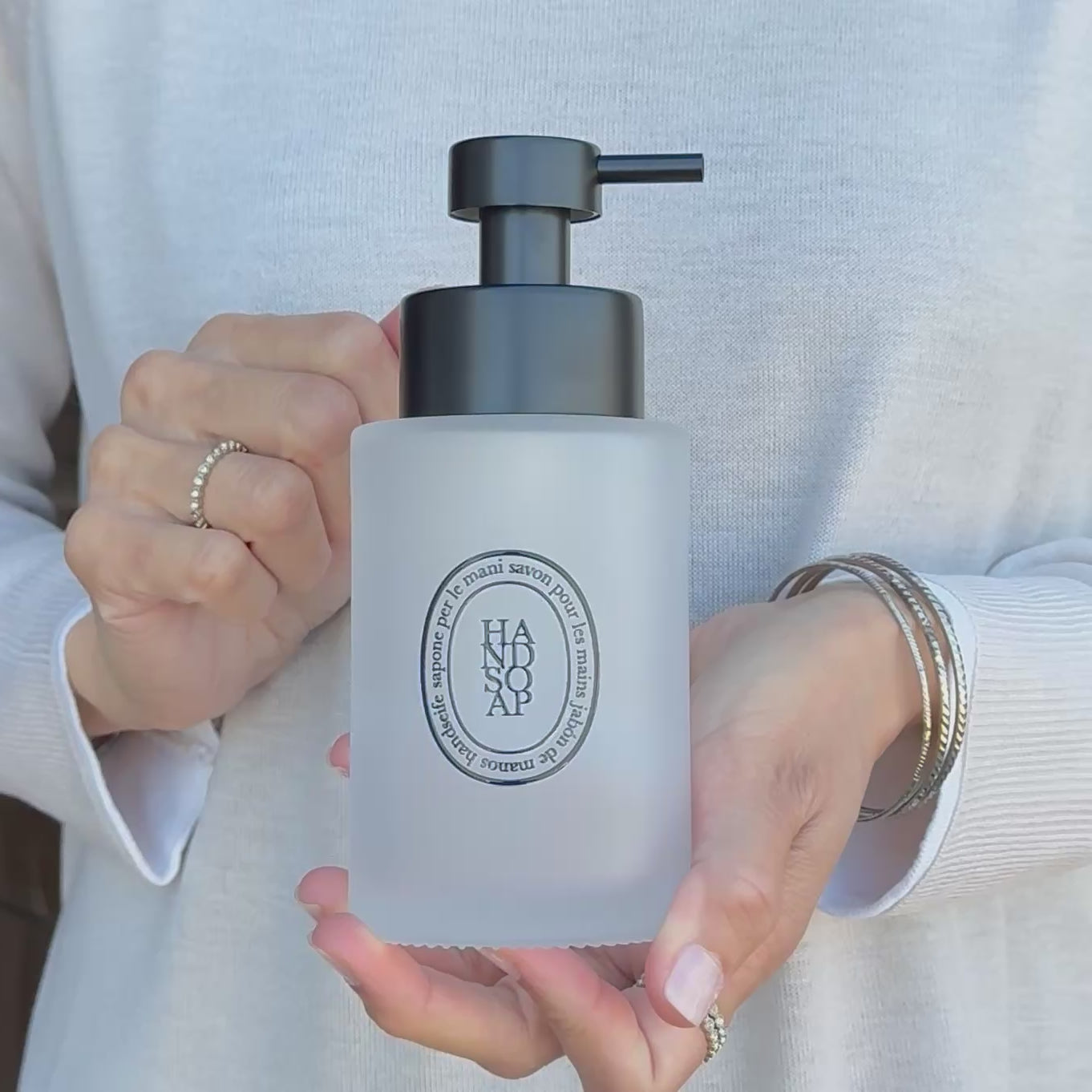 Video showing a frosted glass hand soap dispenser with black oval label and satin black pump, held to demonstrate the size, frosted finish and premium refillable design.