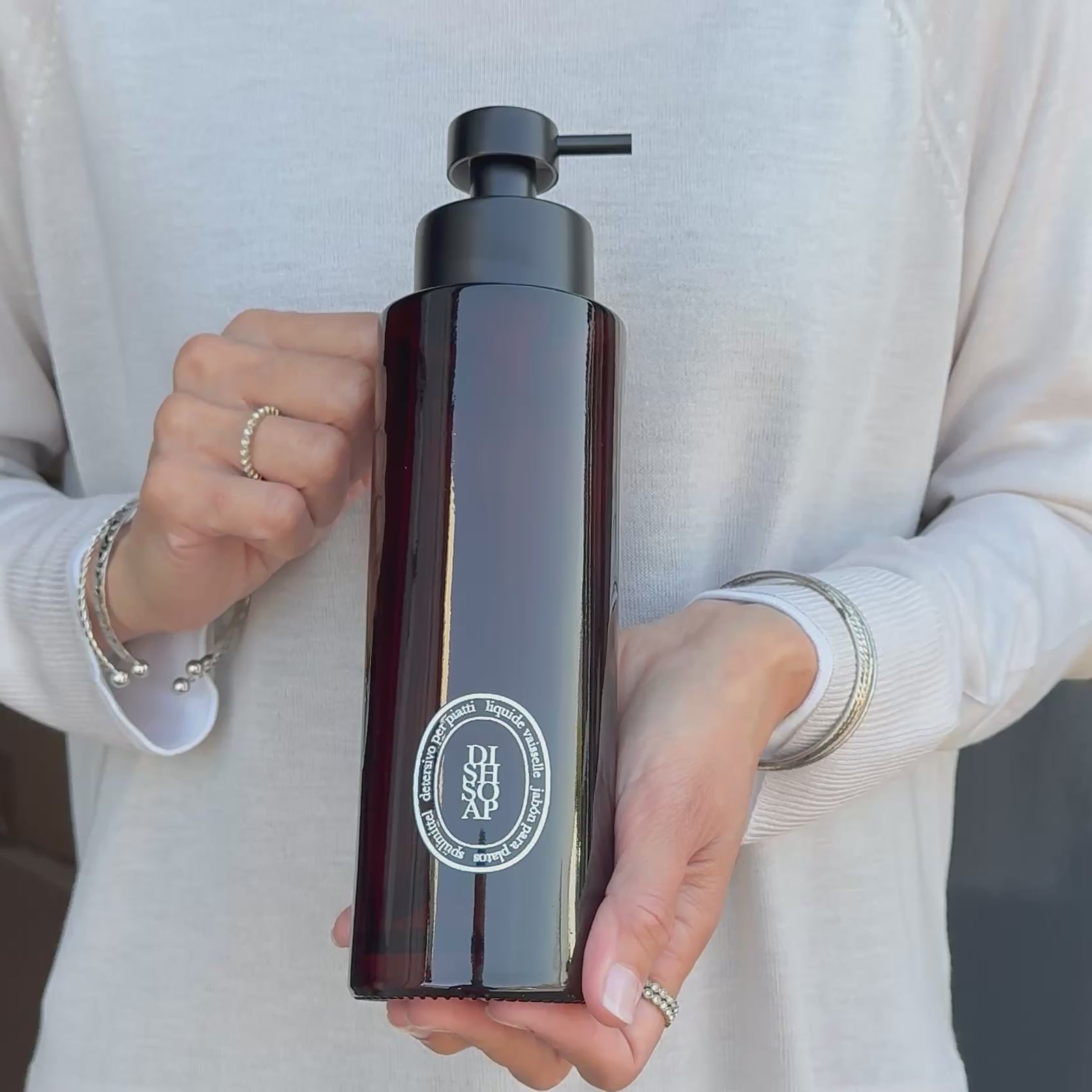 Video showing a 500ml amber glass dish soap dispenser with a white round label and satin black pump, held to demonstrate the bottle’s size, finish and design.