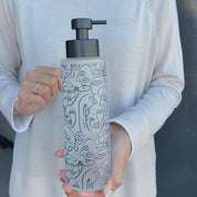 500ml frosted glass soap dispenser with black abstract face line art and satin black pump, shown held in hand to demonstrate the tall refillable bottle size and decorative bathroom design.