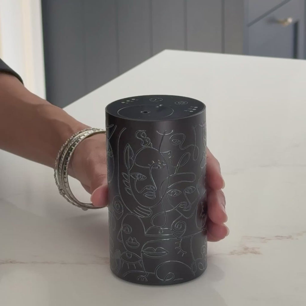 Video close-up of the Loopa black waterless essential oil diffuser showing its top control panel, fragrance outlet and abstract grey line art design. Compact cordless rechargeable aromatherapy diffuser demonstrated by hand on a white countertop, ideal for bedrooms, bathrooms and living spaces.