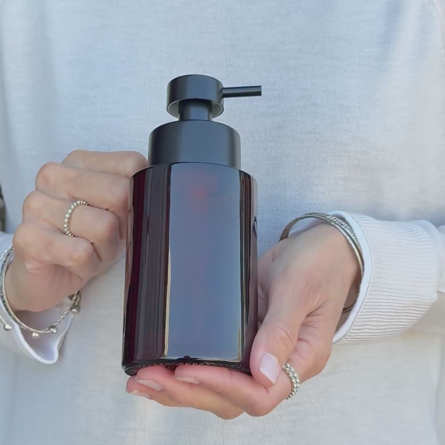 Product video showing a 500ml amber glass refillable soap dispenser being held to demonstrate its tall bottle shape, thick glass construction and satin black stainless steel liquid pump.