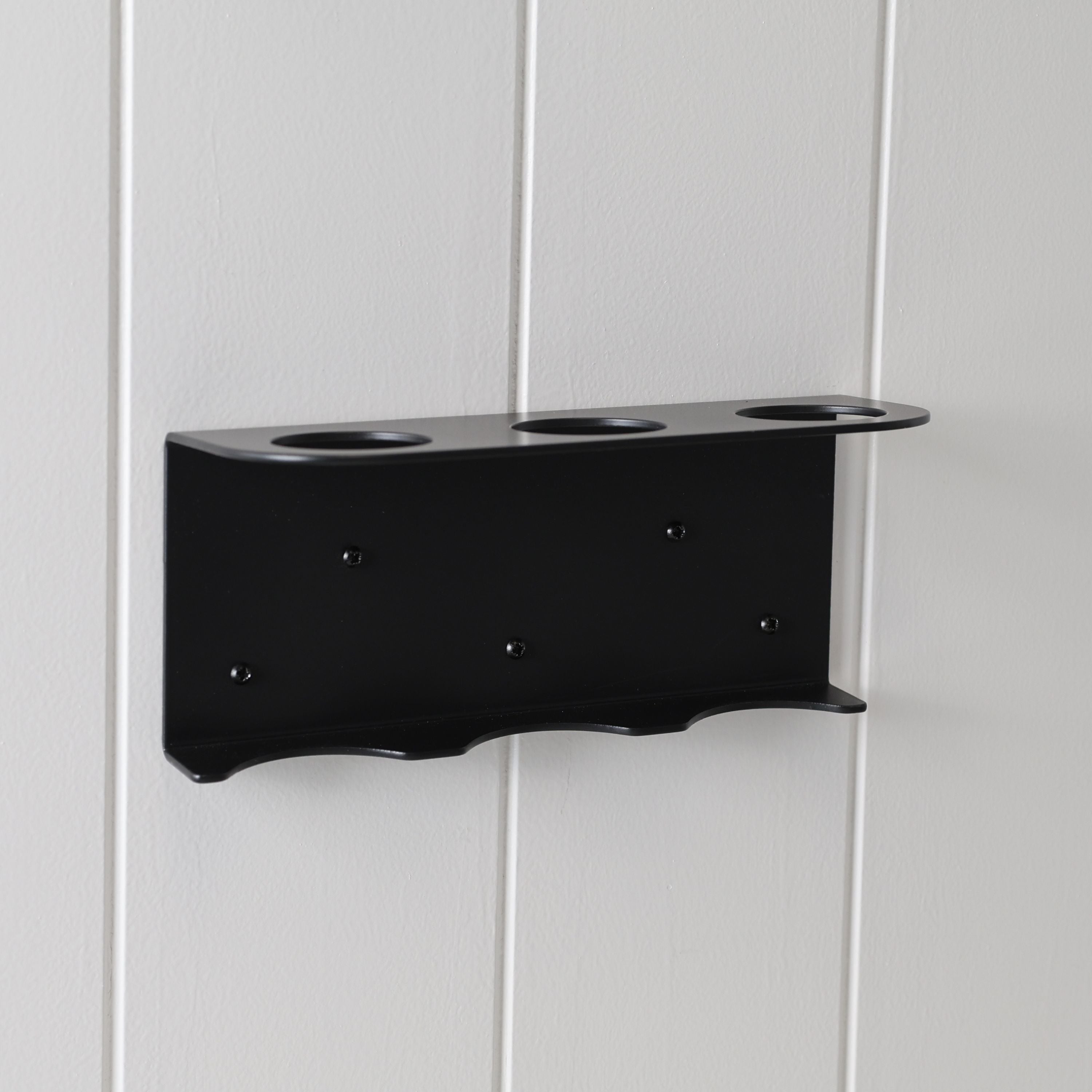 Loopa triple wall-mounted soap dispenser holder in black powder-coated aluminium, securely fixed to a white panelled wall. Featuring three circular bottle openings and a sturdy supporting base, this minimalist bracket accommodates three Loopa 250ml or 500ml refillable dispenser bottles. Ideal for organising shampoo, conditioner and body wash in modern bathrooms and showers.