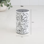 Loopa white waterless essential oil diffuser with black abstract face line art, showing its compact dimensions of 12cm height and 7cm diameter. The cylindrical metal diffuser features a black top control panel and a modern decorative finish. This portable, cordless rechargeable aromatherapy diffuser is designed for convenient placement on bedside tables, desks, shelves and other small spaces.