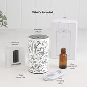 Loopa white waterless essential oil diffuser with black abstract face line art, displayed with all included accessories. The set contains a rechargeable metal aromatherapy diffuser, 20ml amber essential oil bottle, USB charging cable, spare tube, operating manual and packaging box. A complete cordless home fragrance diffuser set, ready to use with your chosen essential oil.